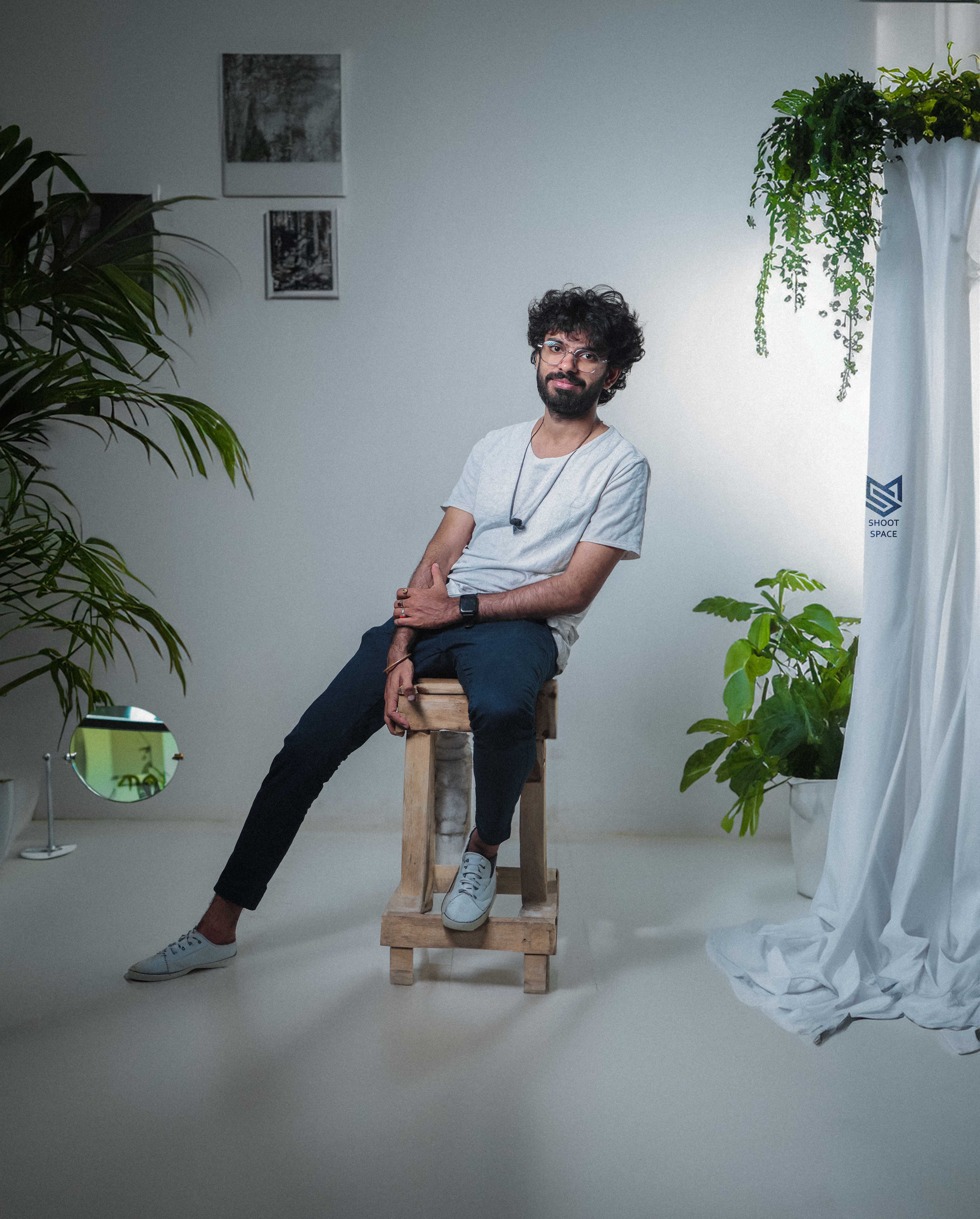 Varun seated on a wooden stool in a plant-filled studio