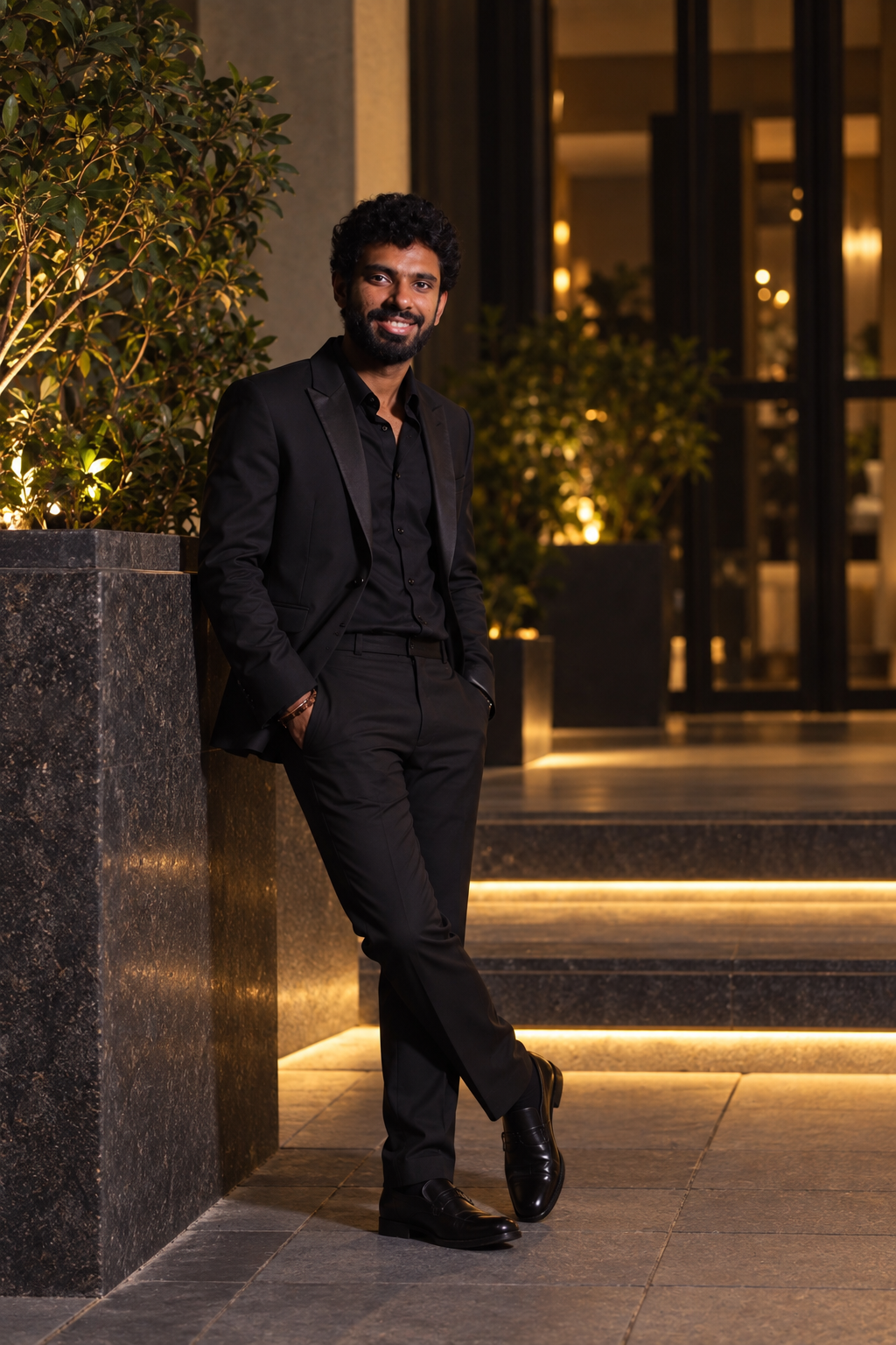 Varun in a black suit, standing beside warmly lit steps